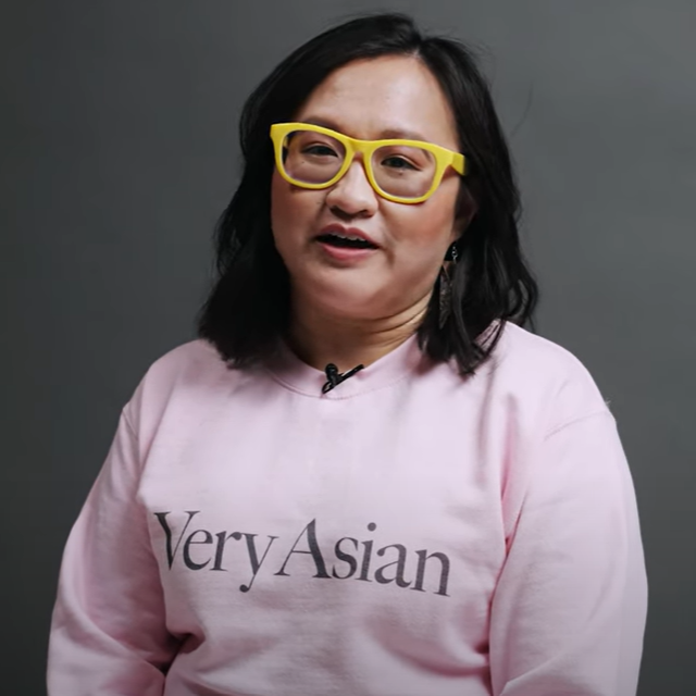 Portrait photo of Linda Hoang, wearing a pink shirt that says 'Very Asian'. Background is grey.