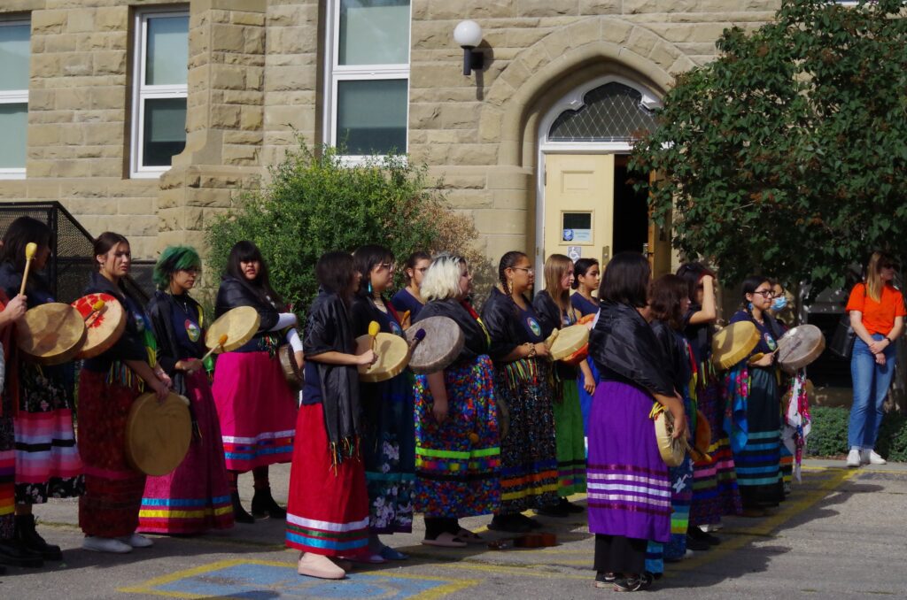 A group of Indigenous women from Stardale Women's Group stand outside a building, drums in hand.