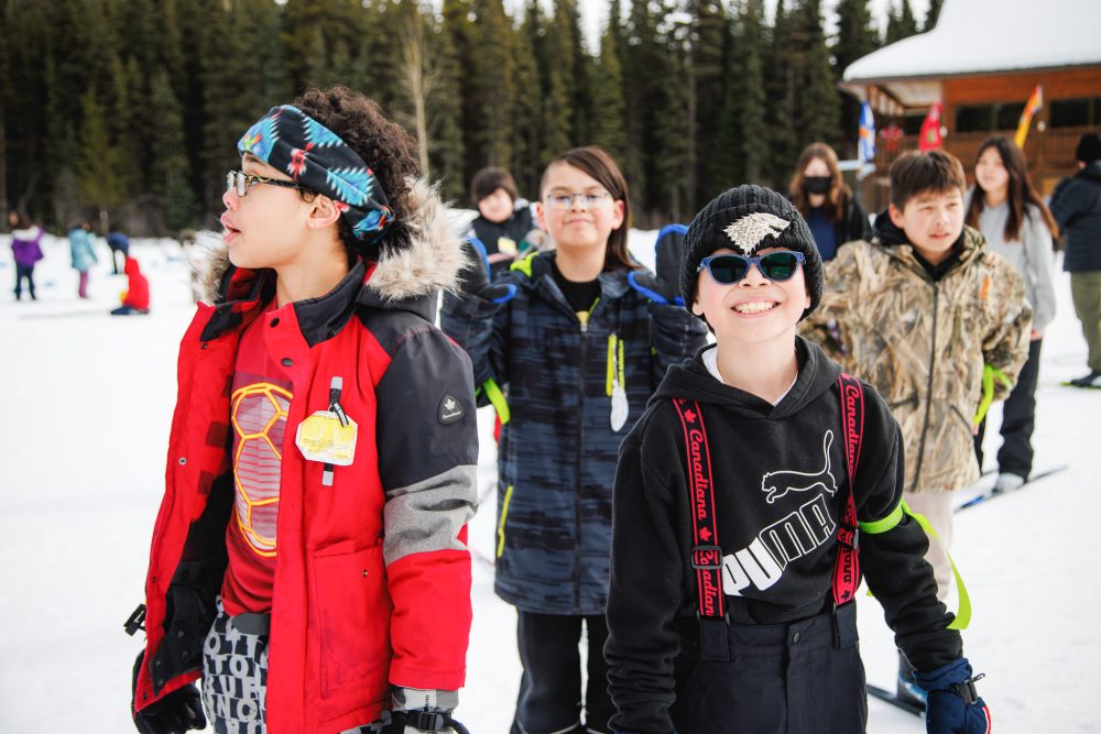 Young children playing and smiling in the snow. | Des jeunes enfants jouent dans la neige en souriant.